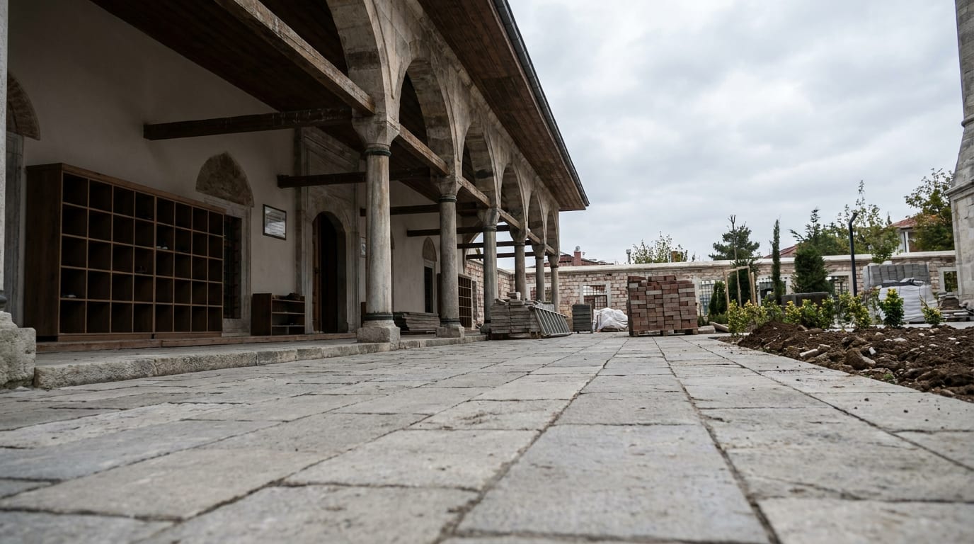 Açık gri parke döşeli cami avlusu; bir kenarda gölgeli revak