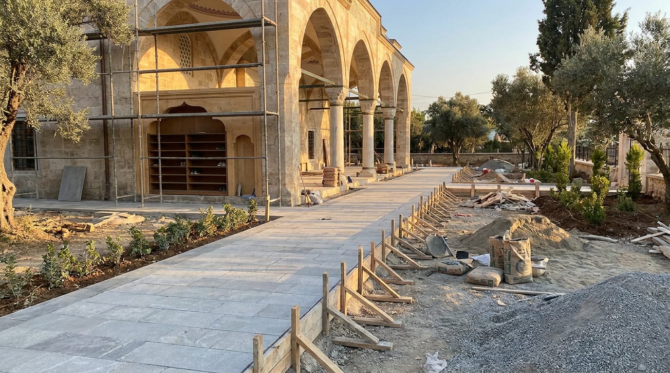 Açık gri parke döşeli cami avlusu; bir kenarda gölgeli revak