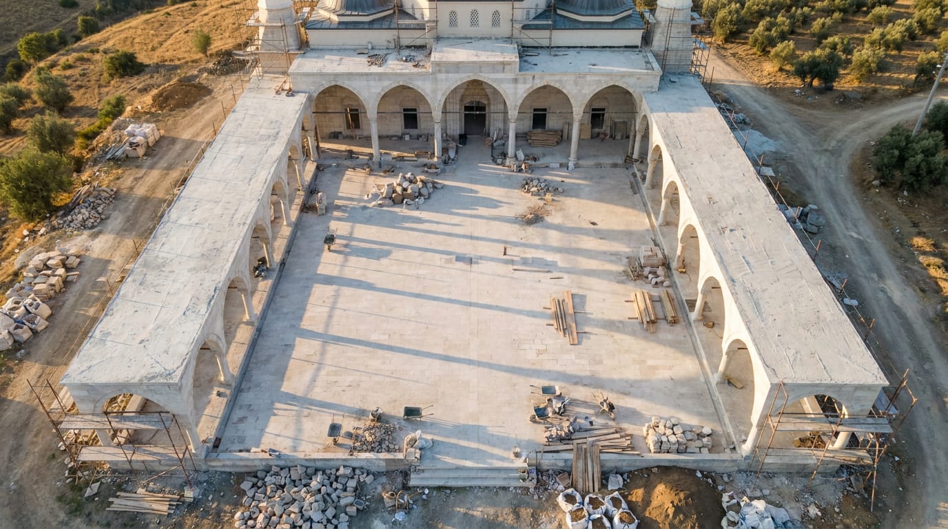 Açık renk parkeyle bitirilmiş cami avlusu; geniş orta alan ve gölgeli revak kenarı